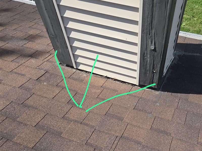 The base of a sided chimney chase with green inspector's lines marking where the flashing has pulled away from the wall.